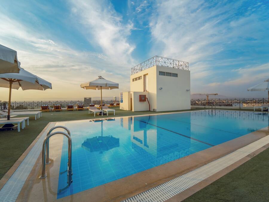 A rooftop pool with clear blue water, surrounded by white umbrellas and lounge chairs.