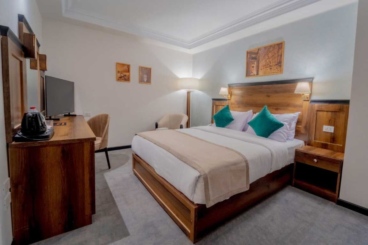 A hotel room with a wooden bed, a desk with a coffee maker, a chair, and a TV.