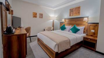 Habitación de hotel con una cama de madera, un escritorio con cafetera, una silla y un televisor.