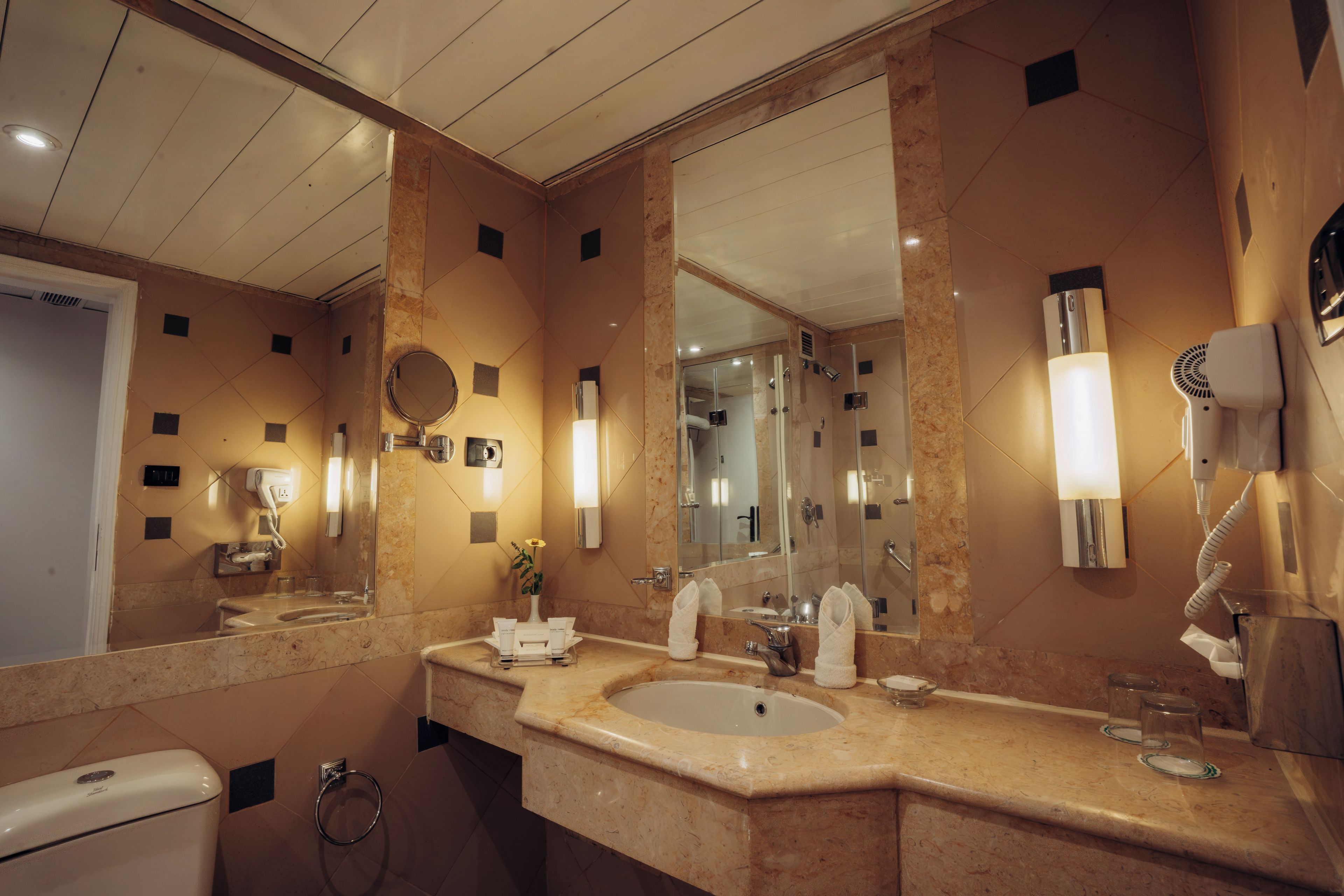 A hotel bathroom with a large mirror, a sink, a hairdryer, and a towel rack.