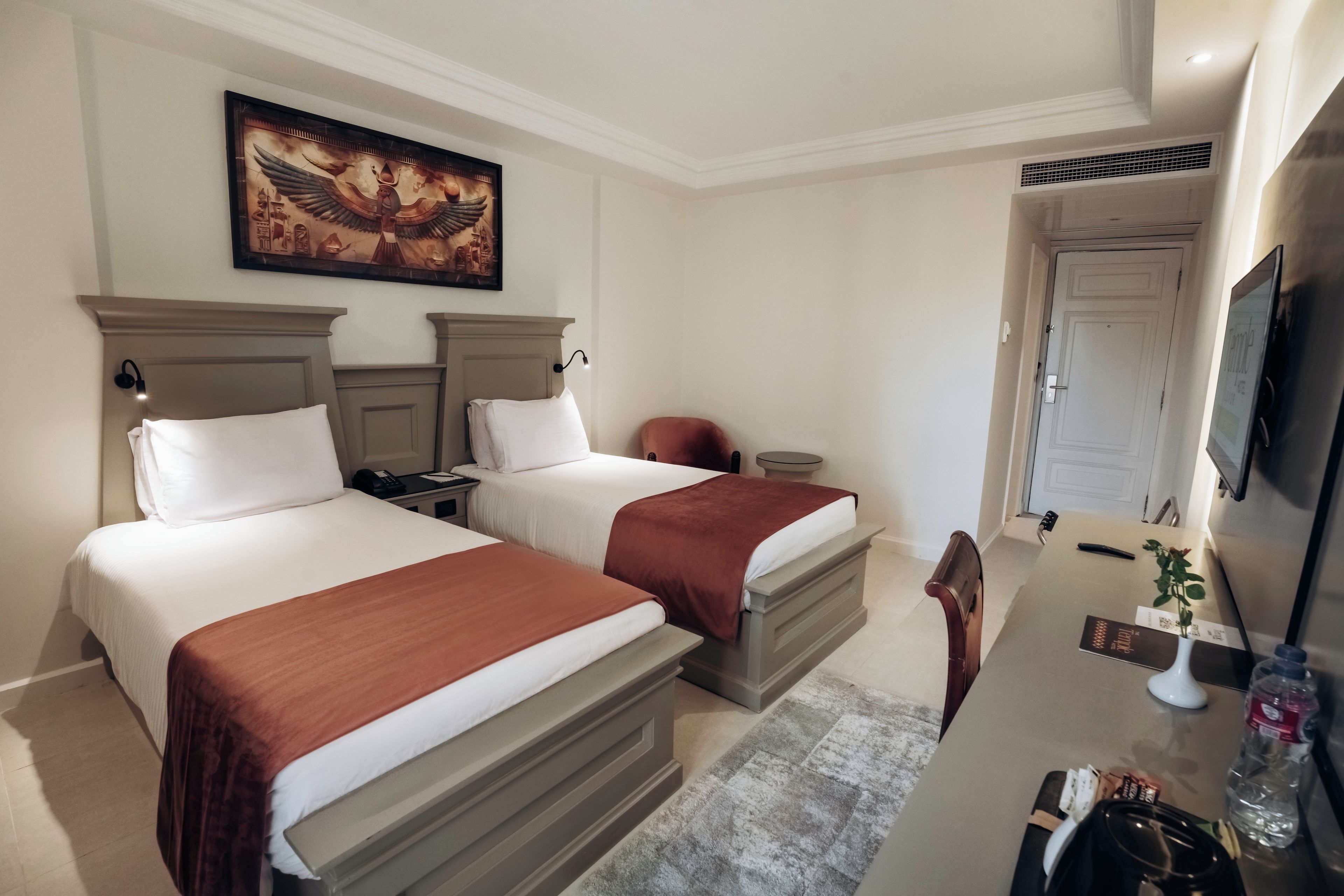 Habitación de hotel con dos camas, un escritorio, una silla, un televisor y un cuadro en la pared.