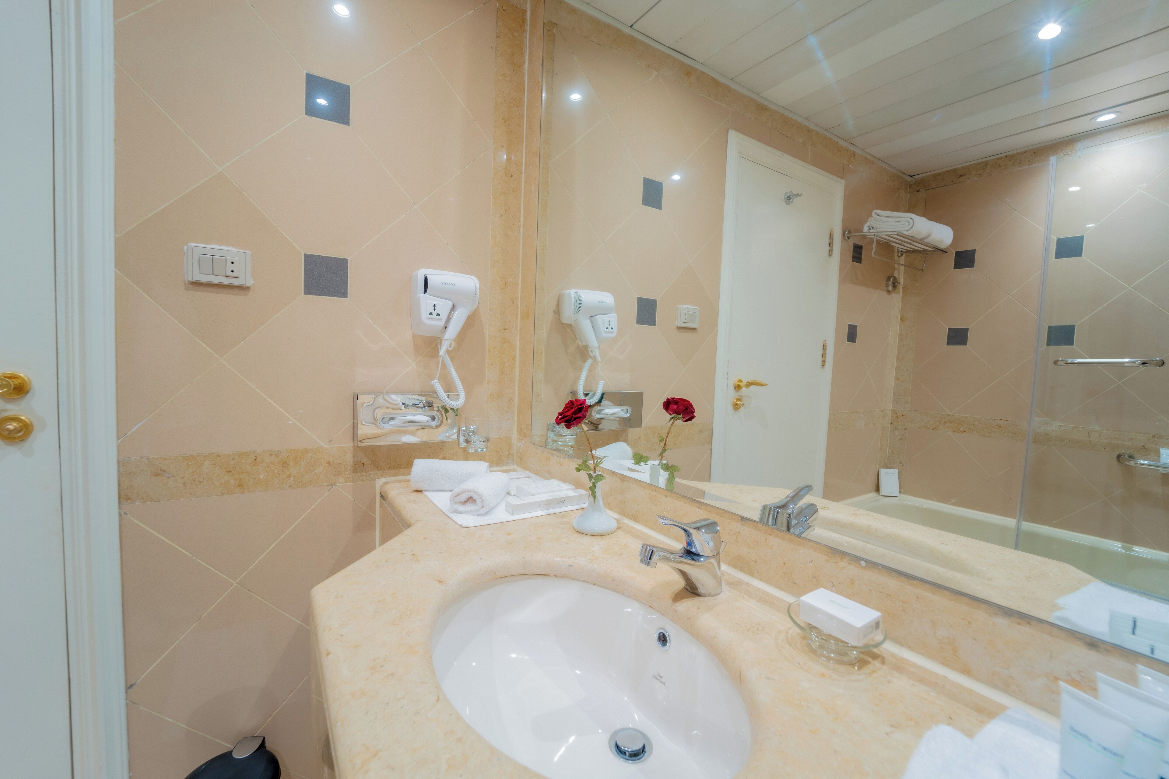 A bathroom with a sink, mirror, towel rack, and a shower area.