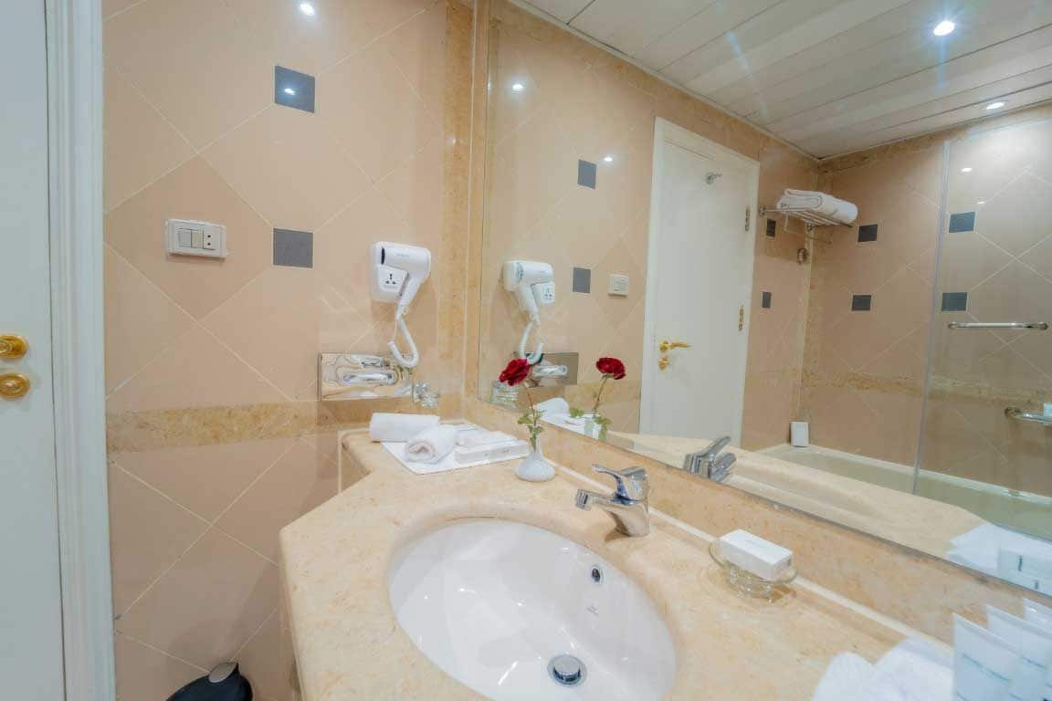 Un baño con lavamanos, espejo y dos secadores de pelo en la pared.