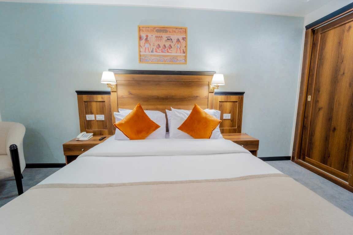 A hotel room with a large bed, two nightstands, a wooden headboard, and a wall-mounted picture.