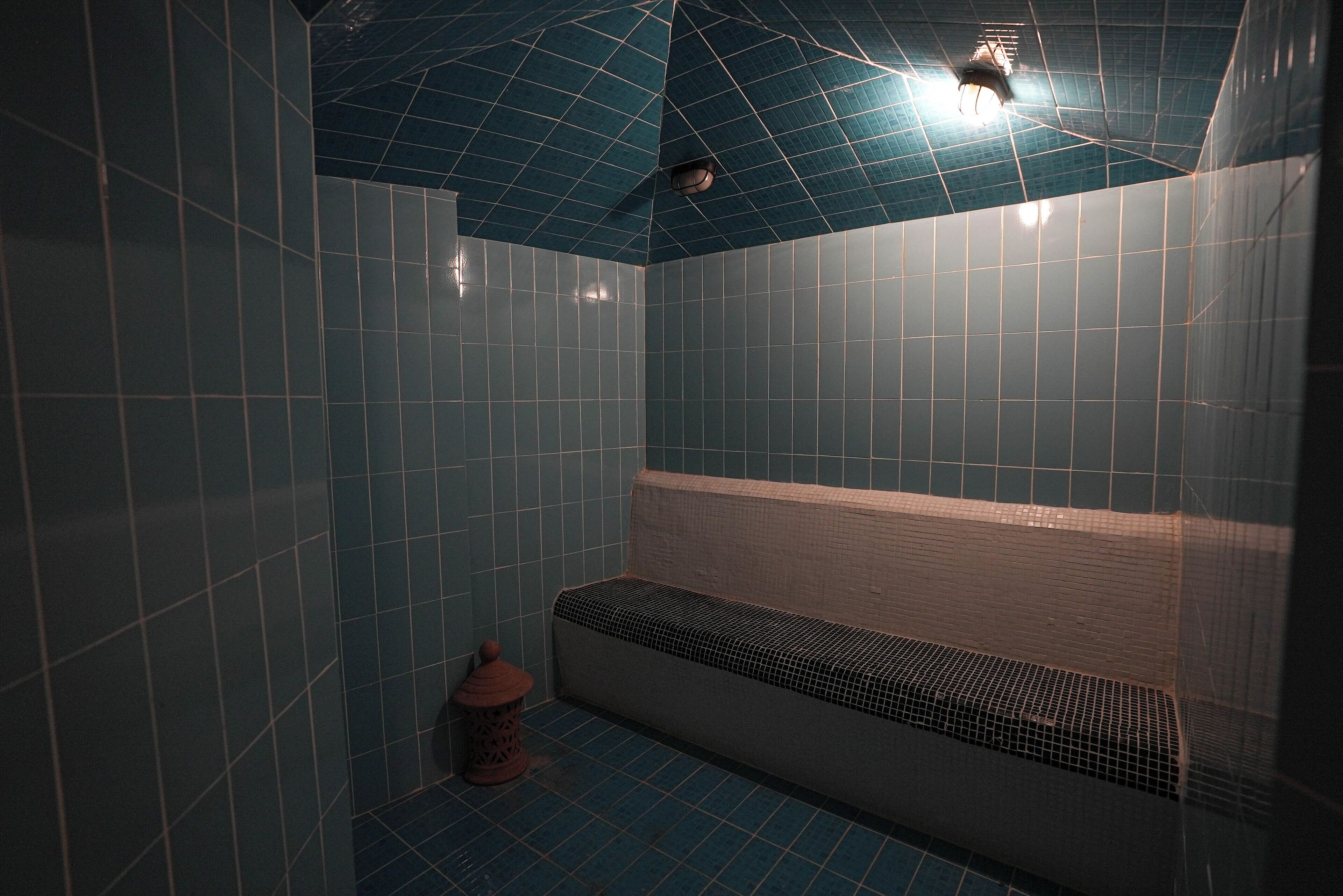 A bathroom with blue tiled walls and a bench.