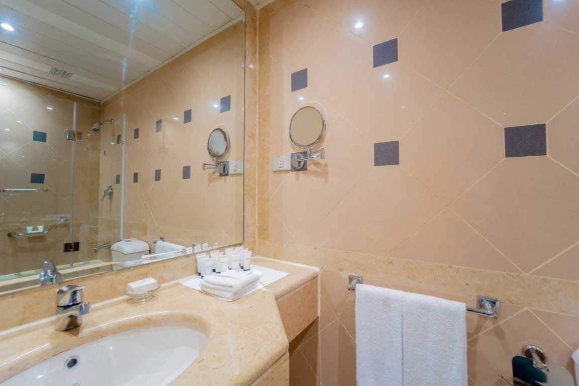Un baño con un espejo grande, un lavamanos con artículos de aseo y un perchero para toallas.