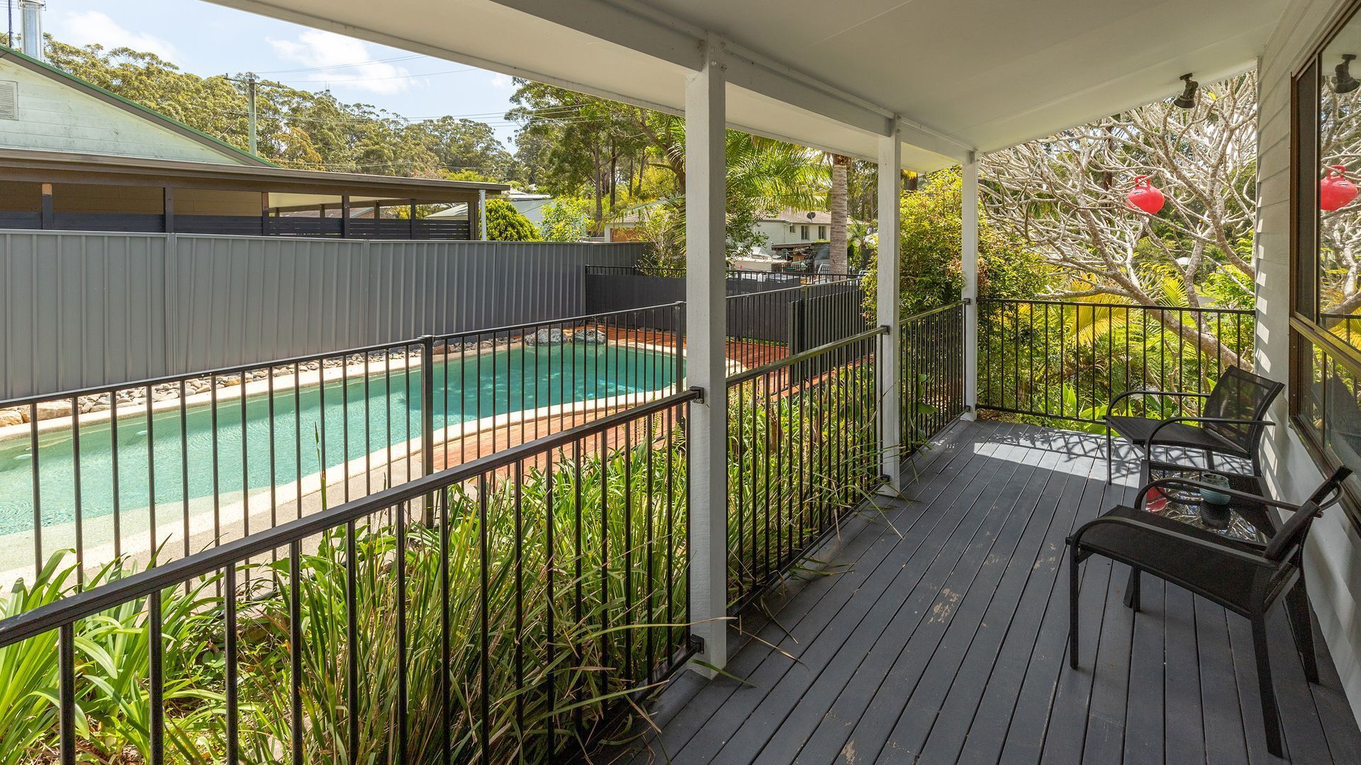 A covered outdoor area with a pool, surrounded by a metal fence and vegetation.