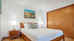Une chambre à coucher avec un lit en bois, deux tables de chevet avec des lampes, une armoire en bois et un tableau coloré accroché au mur.