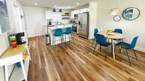 Une cuisine moderne avec des meubles blancs, un réfrigérateur en acier inoxydable et un coin repas avec des chaises bleues et une table en bois.