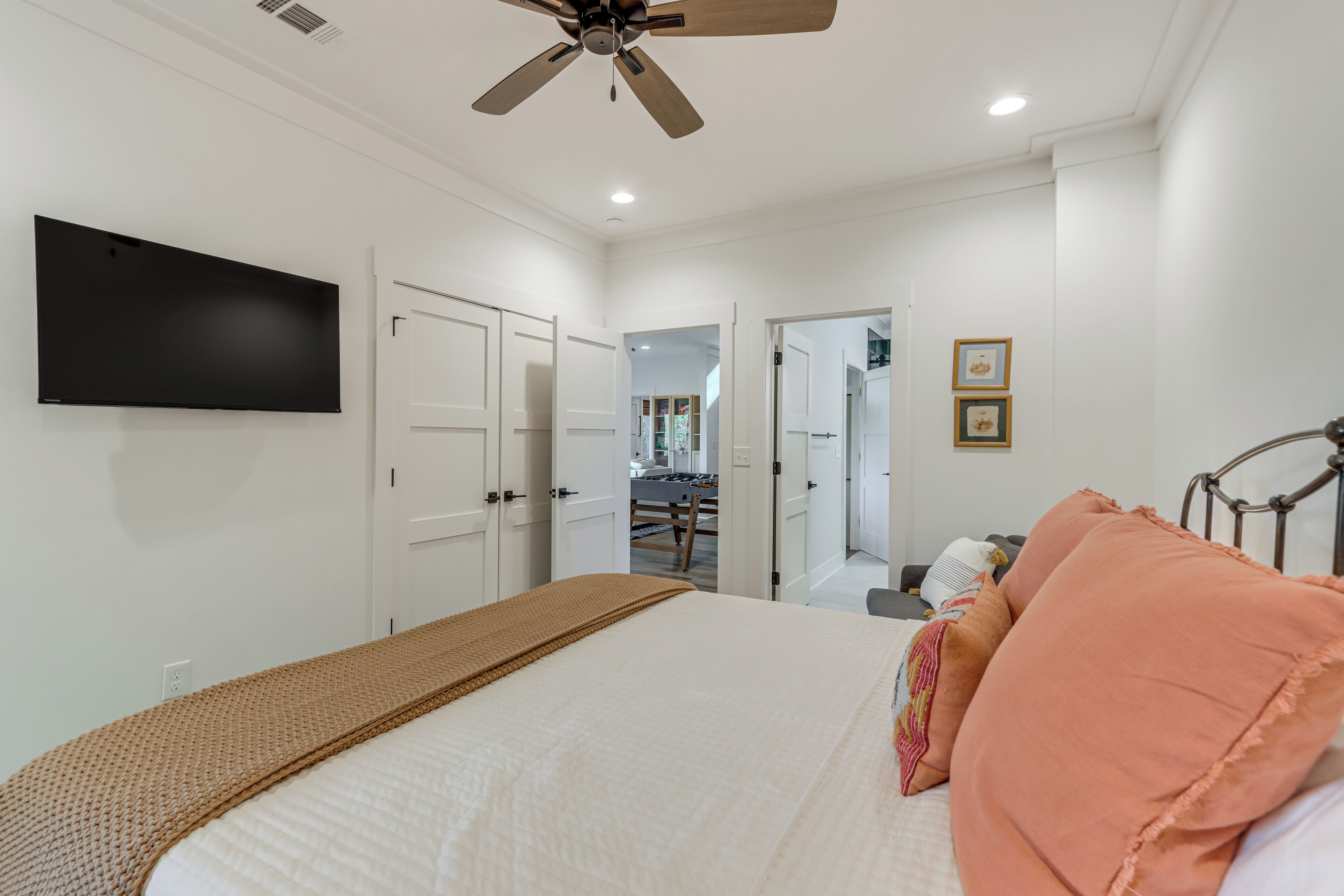 Une chambre à coucher comprenant un lit, un ventilateur de plafond, un téléviseur à écran plat et une porte donnant sur une autre pièce.