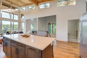 A spacious kitchen with a large island, wooden flooring, and multiple windows offering views of the outdoors.