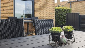 Een terras met een tafel en stoelen, een bakstenen muur, een raam en twee potvazen met vetplanten.