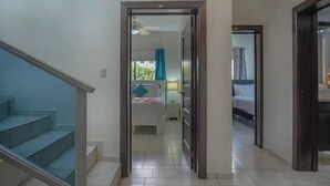 Ein Flur, der in ein Schlafzimmer mit einem Bett, einem Nachttisch und einem mit Vorhängen drapierten Fenster führt.