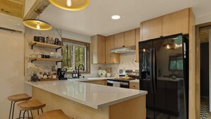 A modern kitchen with a large island, wooden cabinets, a black refrigerator, and bar stools.