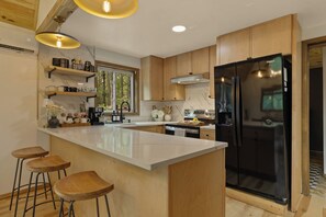 Eine moderne Küche mit einer großen Kochinsel, Holzschränken, einem schwarzen Kühlschrank und Barhocker.