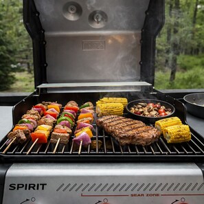 Ein Spirit-Grill mit Fleisch- und Gemüsesticks, ein Steak und Mais am Grill.