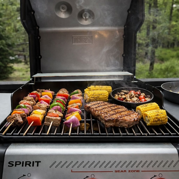 Una parrilla Spirit con brochetas de carne y verduras, un bistec y mazorcas de maíz a la parrilla.