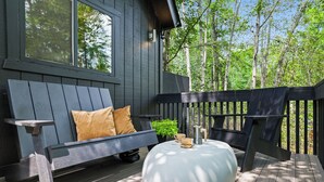 A deck with a wooden bench, a white ottoman, and a coffee maker.