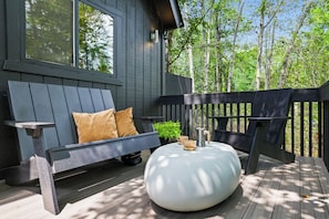 Eine Terrasse mit einer Holzbank, einem weißen Hocker und einer Kaffeemaschine.
