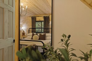 Ein Schlafzimmer mit Bett, Nachttisch, Lampe und einem Fenster mit Vorhängen.