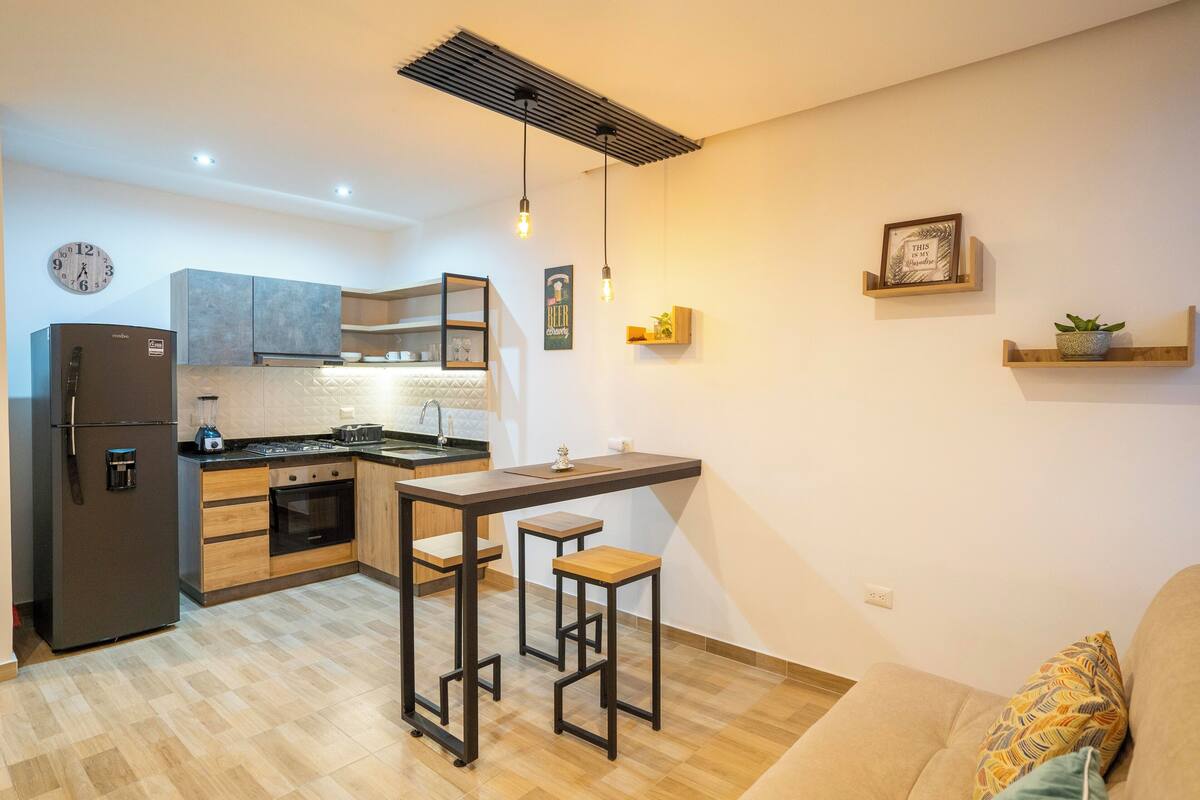 Uma cozinha compacta com forno embutido, geladeira e área de refeições com banquetas.