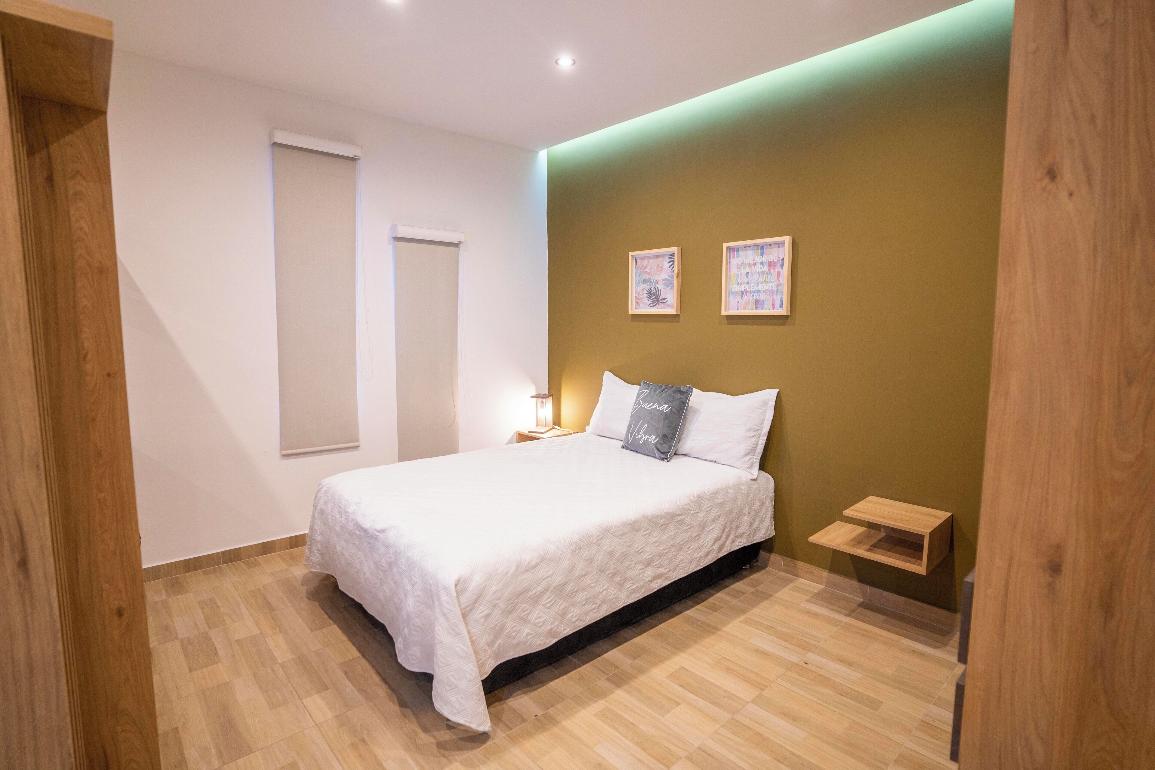 A bedroom with a bed, a nightstand, a wall-mounted shelf, and two framed pictures.