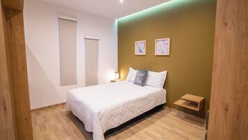 A bedroom with a bed, a nightstand, a wall-mounted shelf, and two framed pictures.