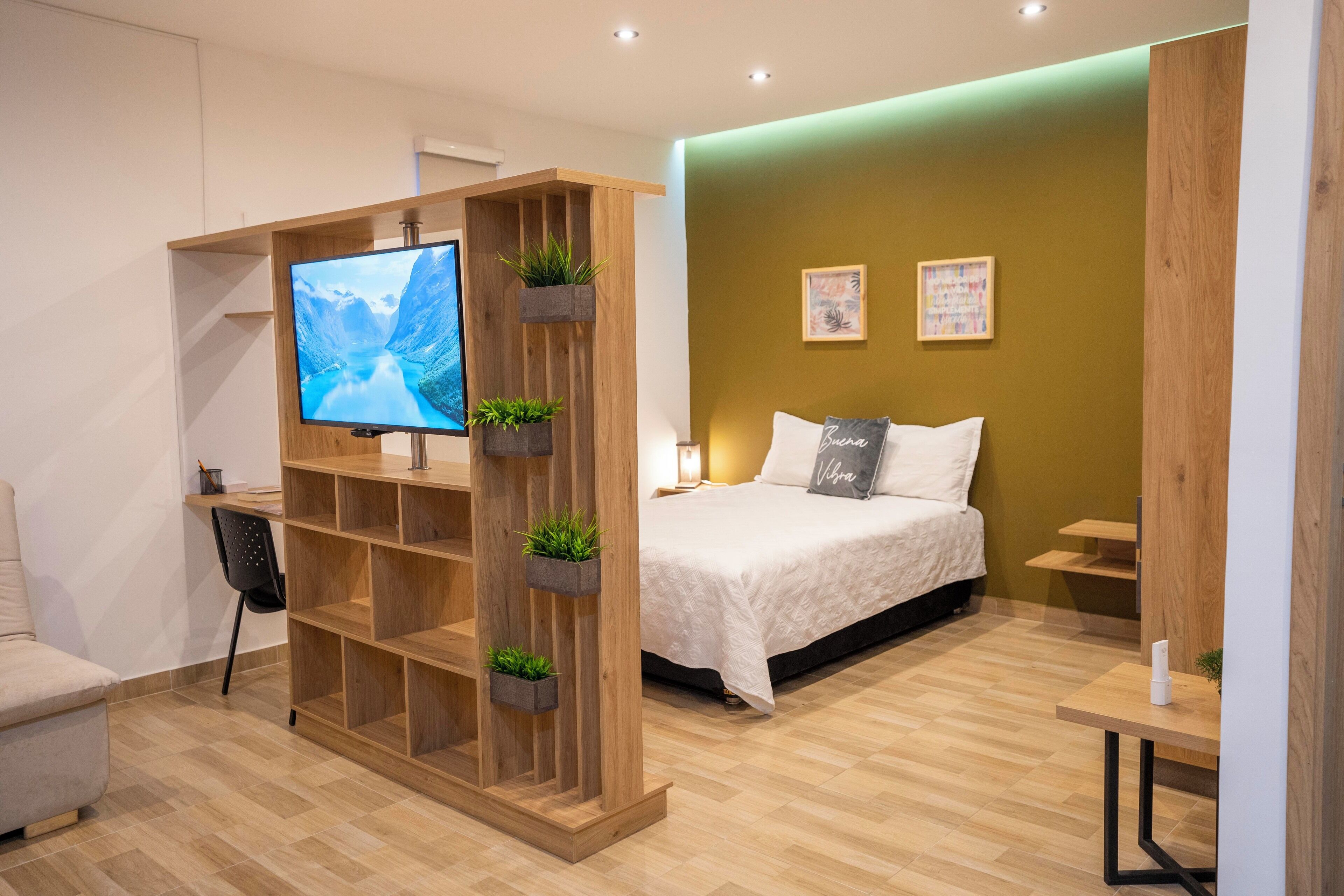Quarto de hotel moderno com uma cama, uma TV fixada em uma prateleira de madeira, uma escrivaninha e uma cadeira.