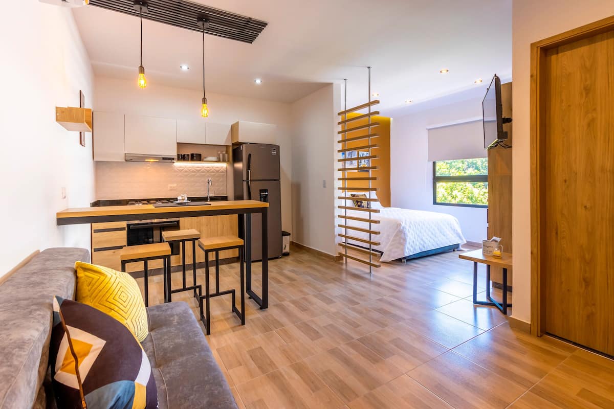 Um espaço compacto com cozinha compacta, um sofá com almofadas, uma cama e uma porta de madeira.