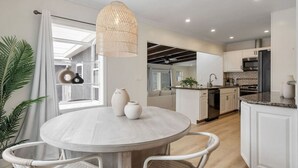 A modern kitchen with white cabinetry, a round dining table, and a hanging light fixture.
