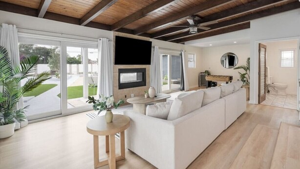 A spacious living room with a large white sofa, a wooden coffee table, and a flat-screen TV mounted on the wall.
