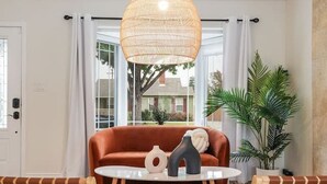 A modern living room with a round wooden coffee table, a brown sofa, a wicker pendant light, and a large window with curtains.