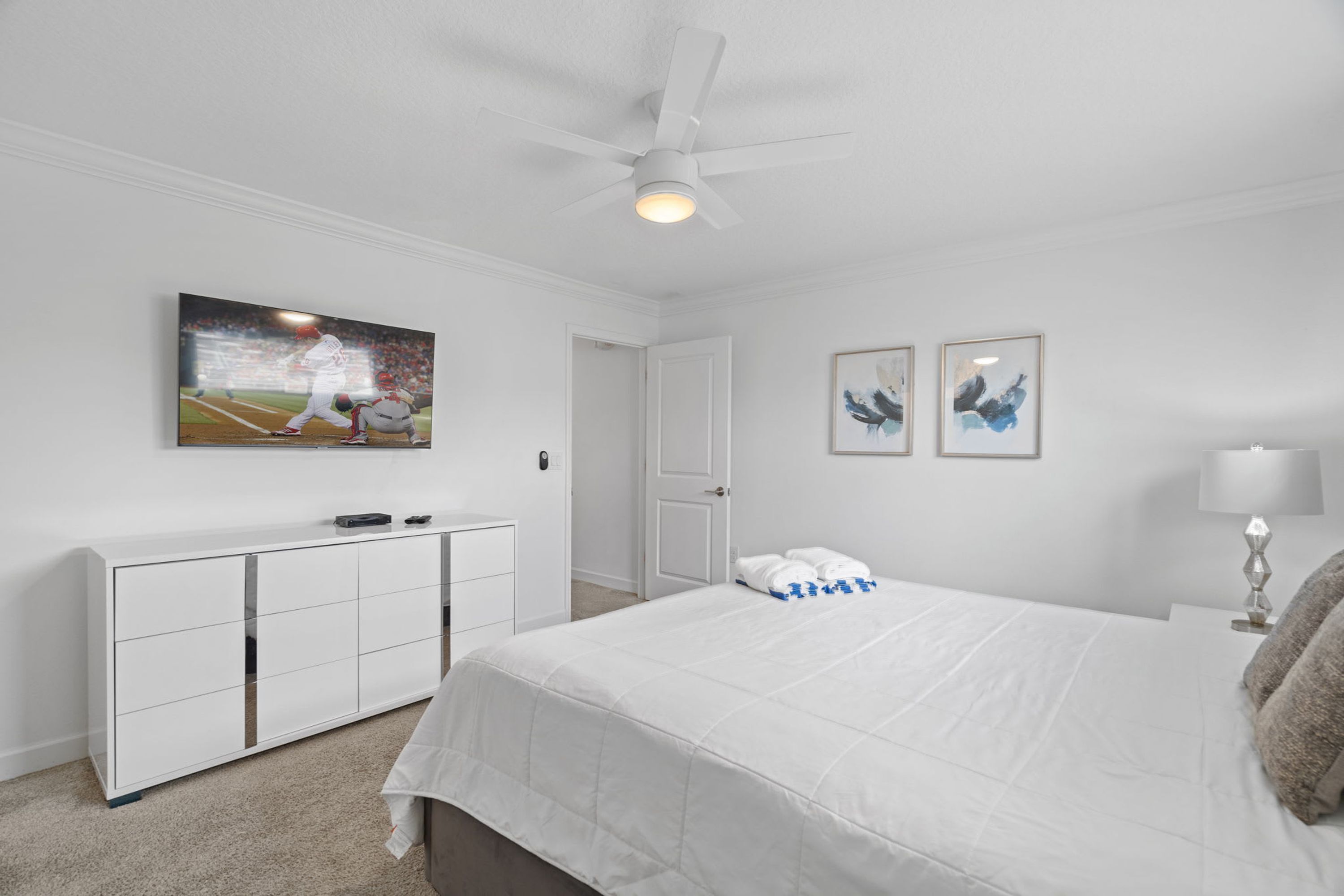 A bedroom with a bed, a white dresser, a ceiling fan, and a painting on the wall.
