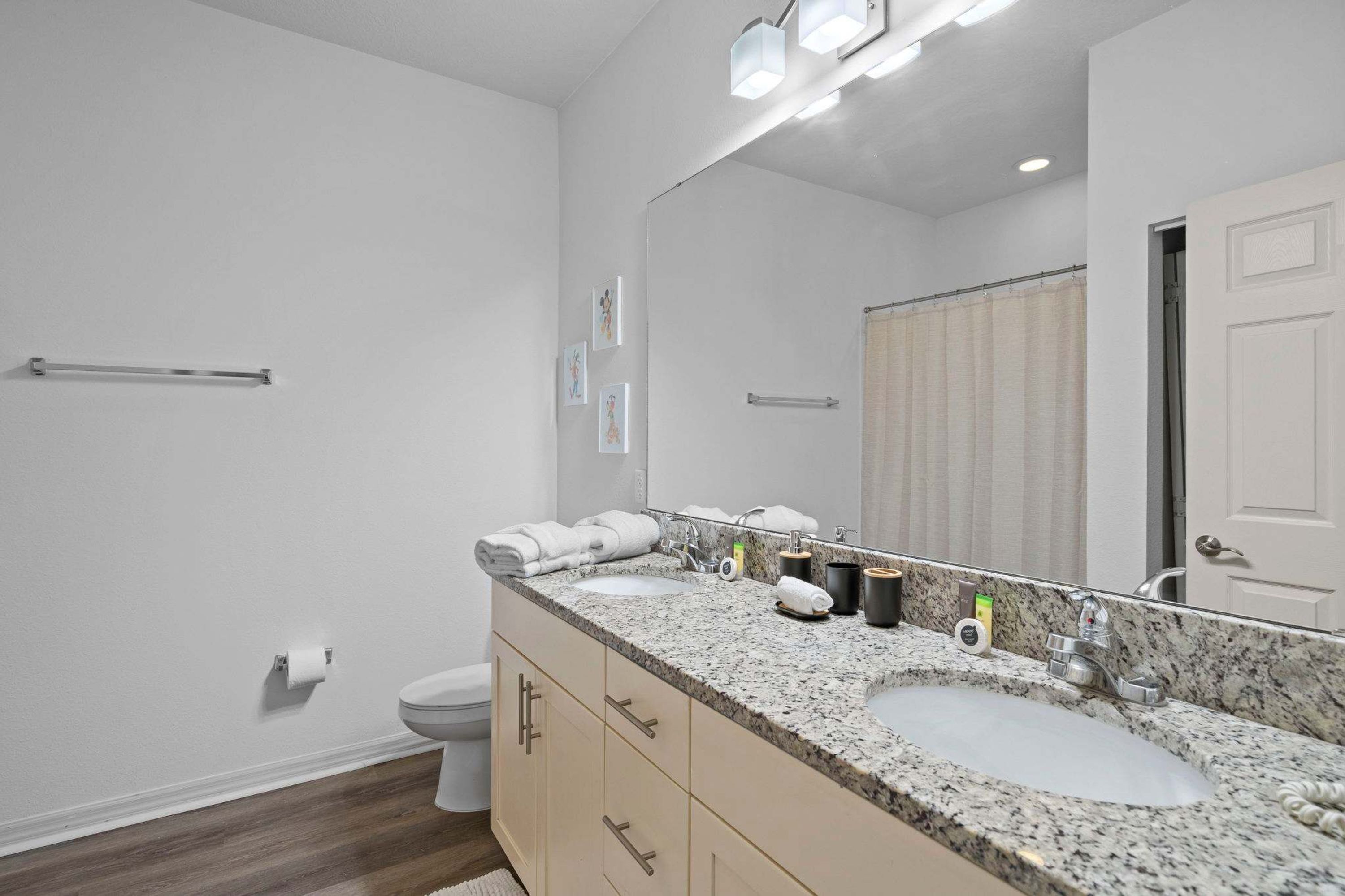 A modern bathroom with a double sink, a large mirror, and a toilet.