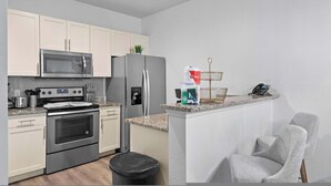 A modern kitchen with stainless steel appliances, white cabinetry, and a granite countertop. - Modern 3 Bed Villa Newly Renovated Prime Location (Kissimmee)