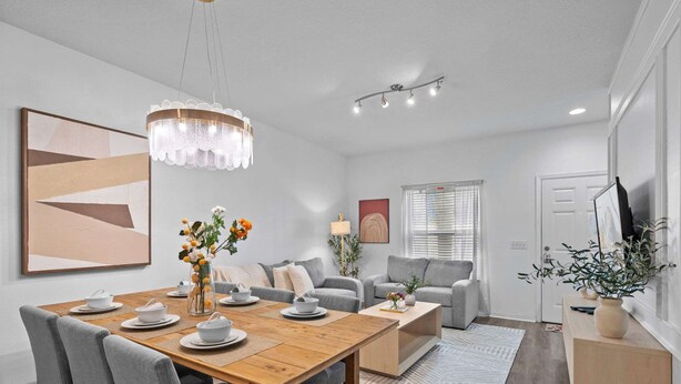 A modern living room with a wooden dining table, grey sofas, and a chandelier. - Modern 3 Bed Villa Newly Renovated Prime Location (Kissimmee)