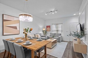 A modern living room with a wooden dining table, grey sofas, and a chandelier. - Modern 3 Bed Villa Newly Renovated Prime Location (Kissimmee)