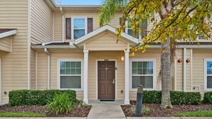 A two-story building with a beige exterior, a brown front door, and a small porch area. - Modern 3 Bed Villa Newly Renovated Prime Location (Kissimmee)