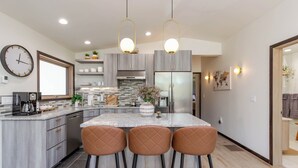 A modern kitchen with a central island, bar stools, a clock, and a refrigerator. - Modern Luxury Retreat - 2 BR/1BA - Minutes from Downtown (Rapid City)