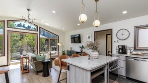 A modern kitchen with a central island, built-in oven, and stainless steel appliances. There are large windows offering a view of greenery outside. - Modern Luxury Retreat - 2 BR/1BA - Minutes from Downtown (Rapid City)