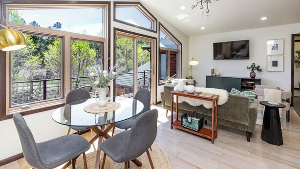 A modern living room with a glass dining table, grey chairs, a sofa, and a TV mounted on the wall. - Modern Luxury Retreat - 2 BR/1BA - Minutes from Downtown (Rapid City)