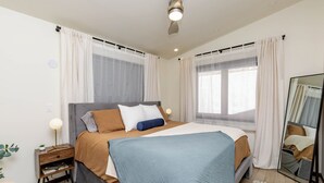 A modern bedroom with a large bed, bedside tables, a mirror, and a view of the outdoors. - Modern Luxury Retreat - 2 BR/1BA - Minutes from Downtown (Rapid City)