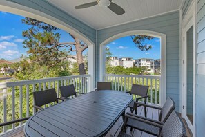 A covered outdoor patio with a table and chairs, surrounded by a white railing, overlooking a residential area with houses and trees. - Just Shellin' - Santa Rosa Beach, Walk to Shops + Dining, Walk to Beach! (Santa Rosa Beach)