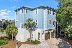 A multi-story residential building with a garage, a driveway, and a landscaped front yard. - Just Shellin' - Santa Rosa Beach, Walk to Shops + Dining, Walk to Beach! (Santa Rosa Beach)