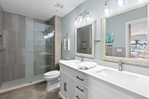 A modern bathroom with a glass-enclosed shower, a white toilet, and a vanity with two sinks and a large mirror.