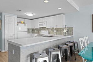 A modern kitchen with white cabinets, a central island, stainless steel stools, and a microwave.