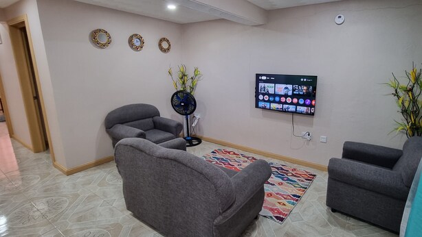 Un soggiorno con divani grigi, una TV a schermo piatto, specchi decorativi a parete e un tappeto con motivo.