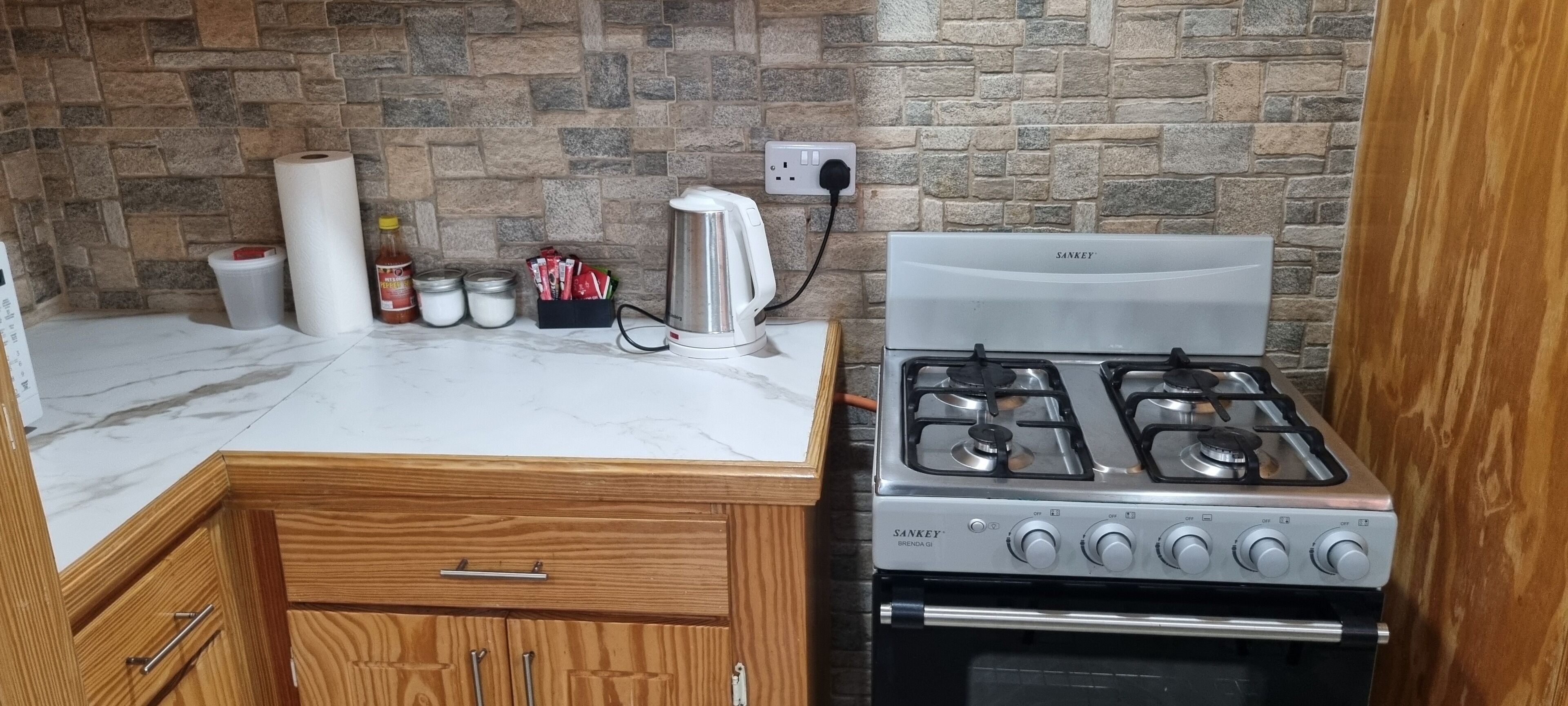 A kitchen with a stone wall backsplash, a white countertop, a stainless steel stove, and wooden cabinets.
