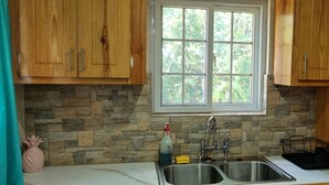 Una cucina con mobili in legno, uno schienale in pietra, un lavello doppio e una finestra vista verde.