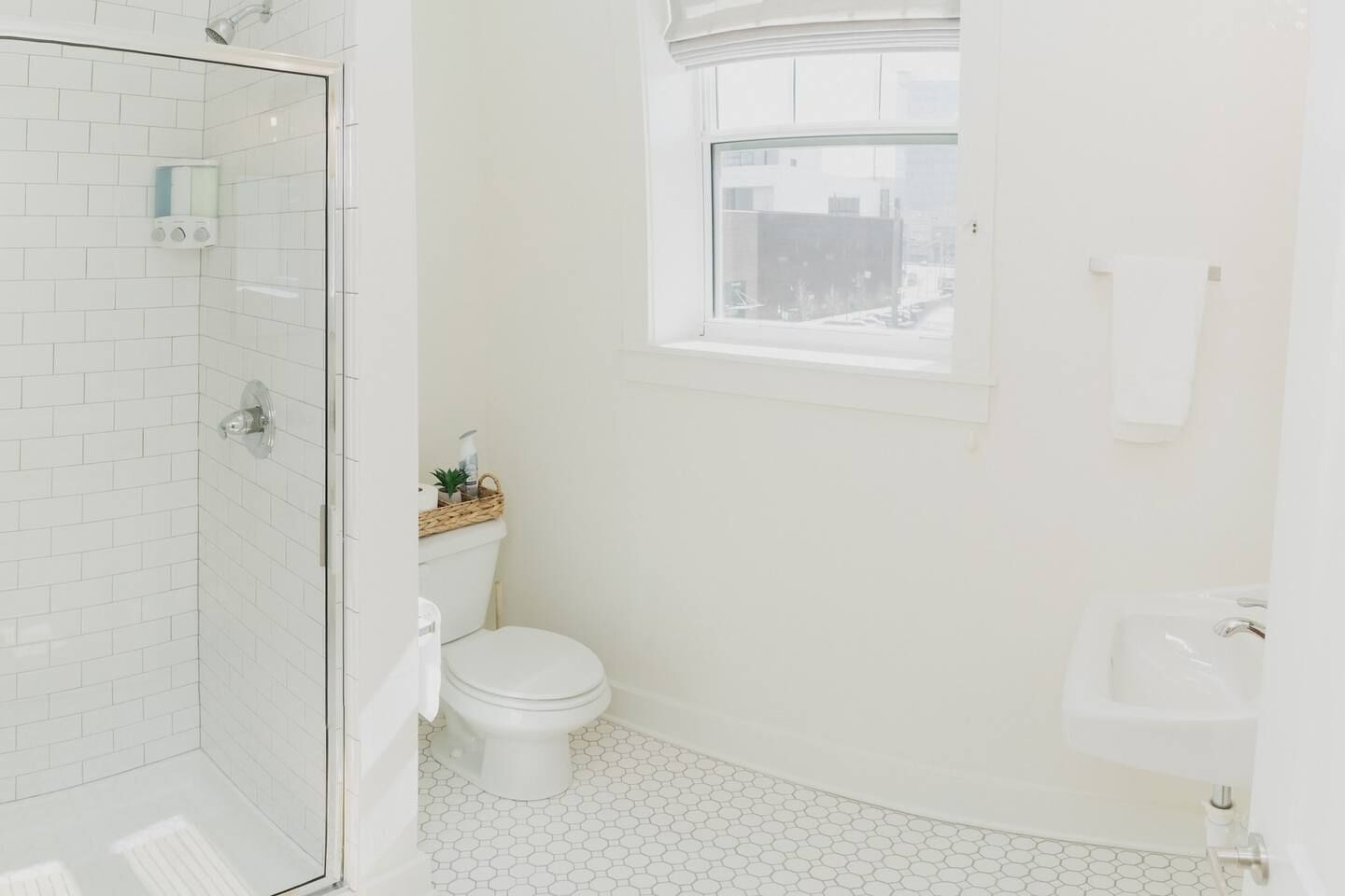A bathroom with a glass shower enclosure, a toilet, a sink, and a window.
